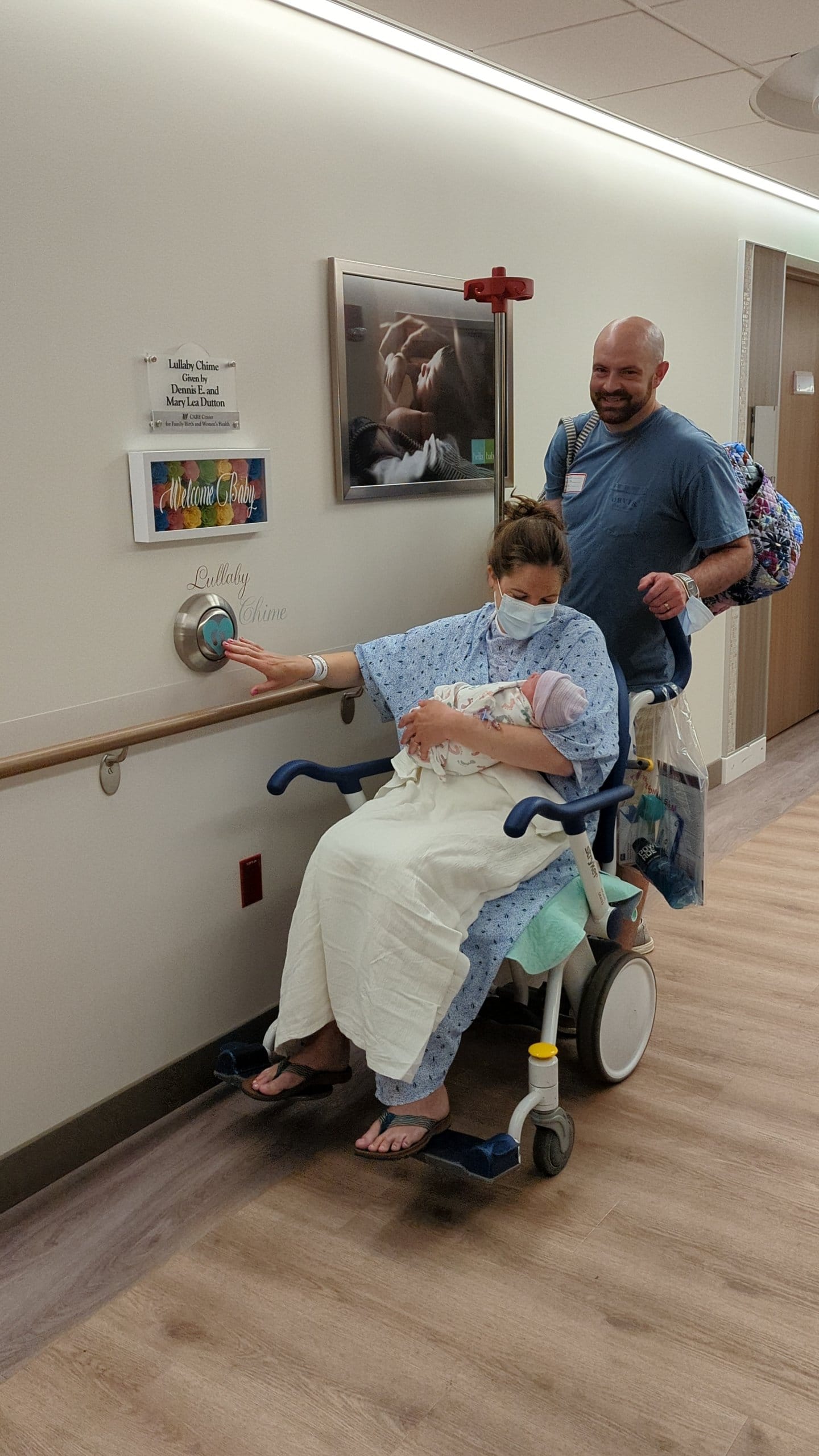WHS patient pushing the lullaby chime button after giving birth. Husband pushing wheel chair. Baby in her arms